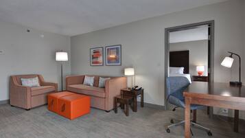 Una habitación de hotel moderna con dos sofás, un reposapiés naranja, un escritorio y una silla.