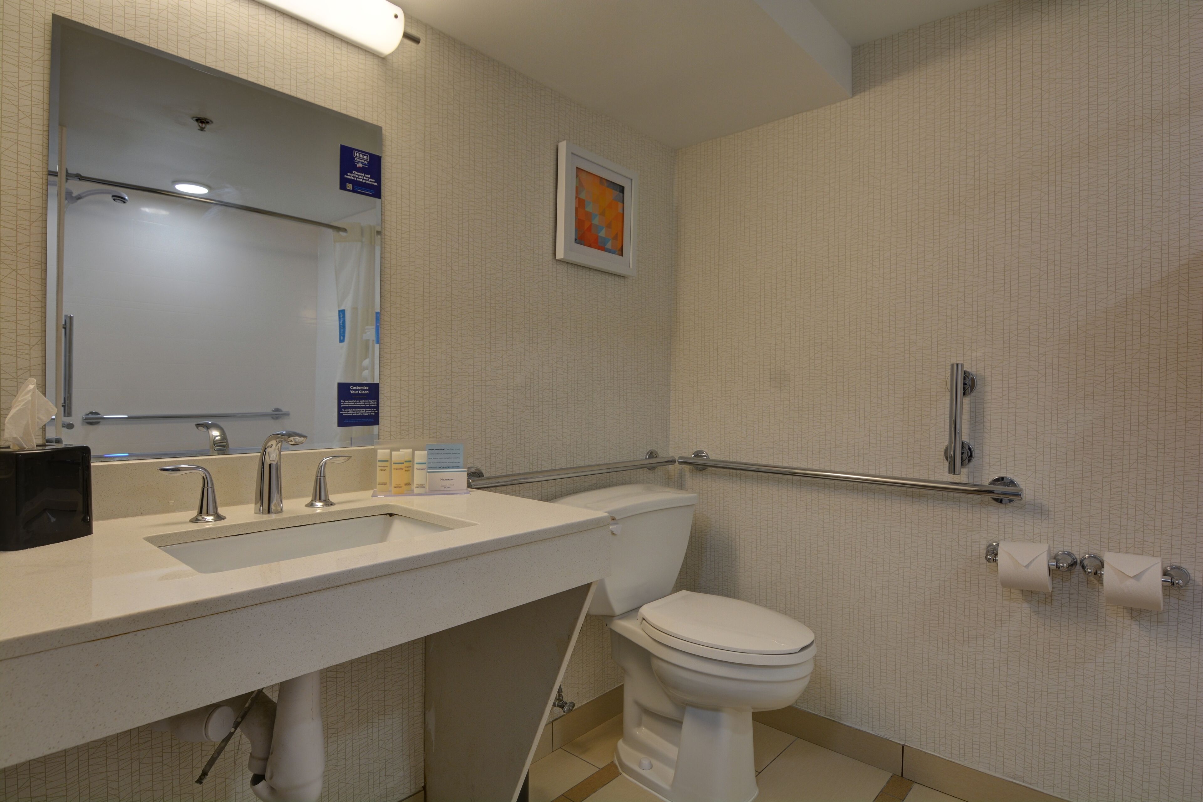 Baño con lavamanos, inodoro y barras de apoyo.