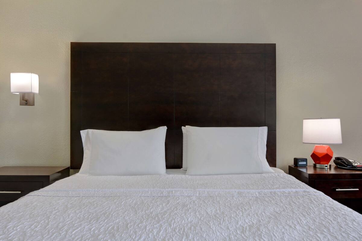 A hotel room with a large bed, two bedside lamps, a nightstand, and a modern headboard.
