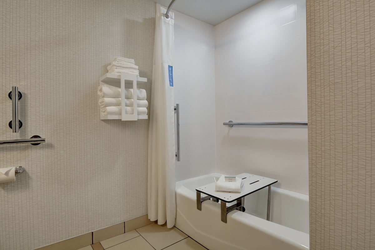 A modern bathroom with a walk-in shower, a bathtub with a small table, and a towel rack.
