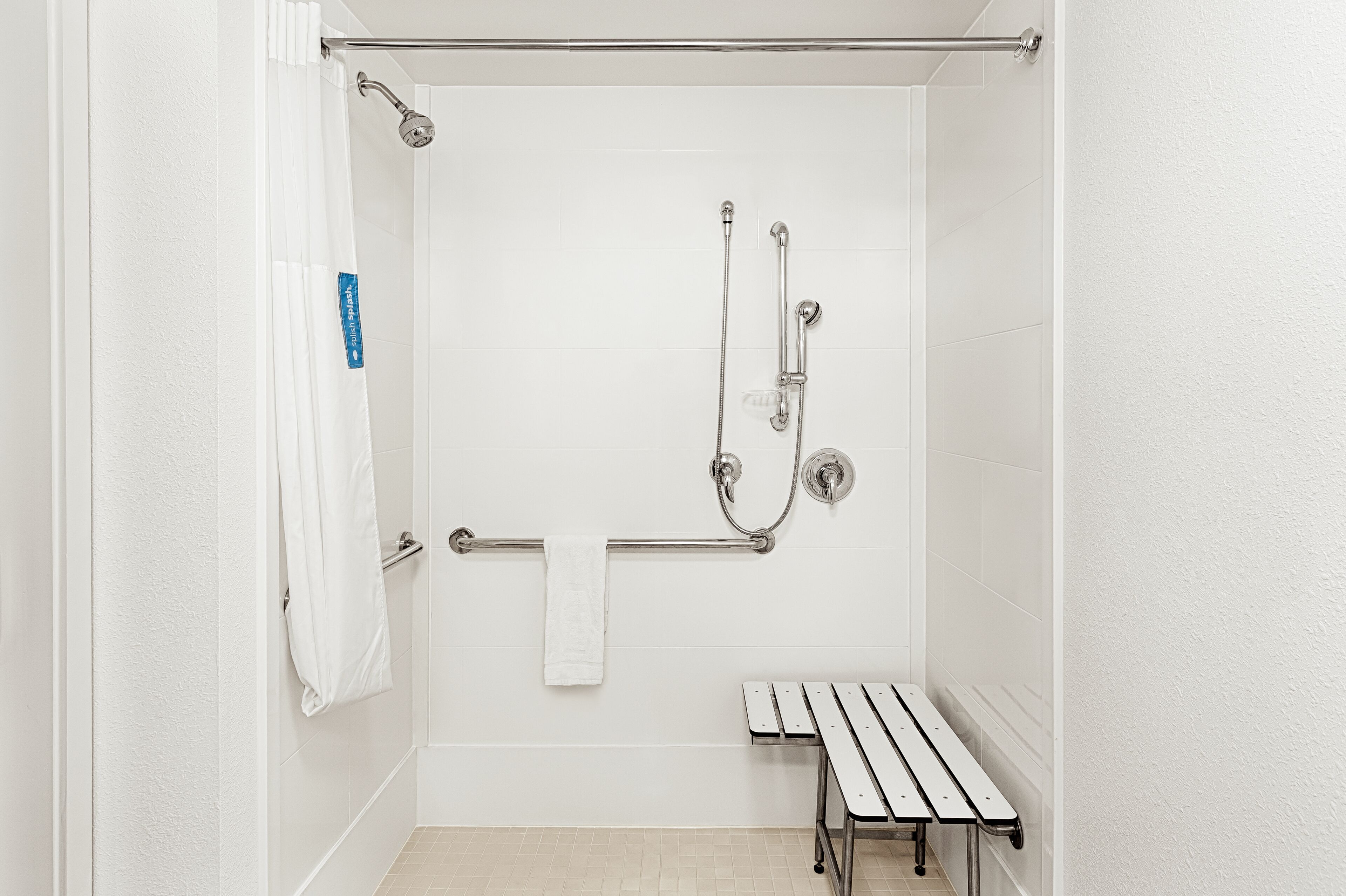 A white bathroom with a shower, grab bar, and bench.