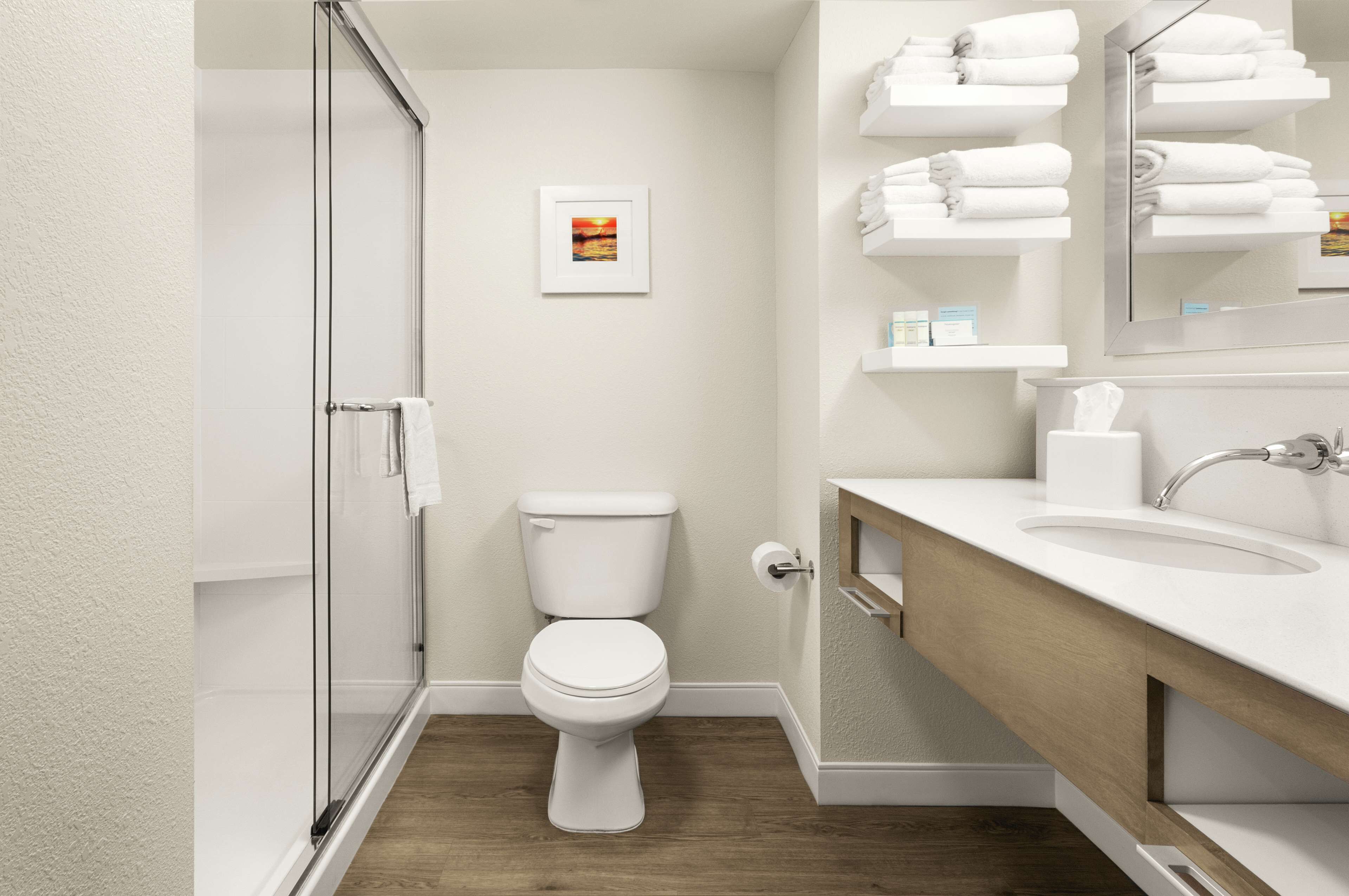 Une salle de bain moderne avec une douche à parois de verre, des toilettes blanches, un meuble-lavabo en bois et un miroir.