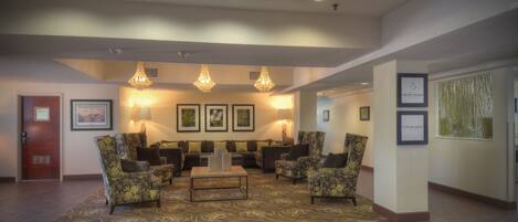 A lobby with a seating area, chandeliers, framed artwork, and a wooden floor.