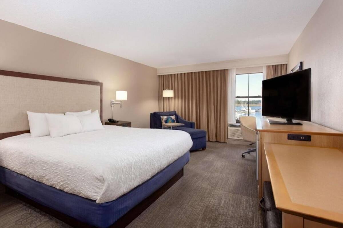 Una habitación de hotel con una cama grande, un escritorio, una silla, un televisor y una ventana con cortinas.