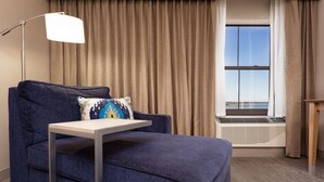Habitación de hotel con sofá azul, una mesita, una ventana con cortinas y un radiador.