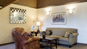 A living room with a brown leather armchair, a gray sofa, a coffee table, a mirror with a checkered pattern, and a framed picture of a landscape. - Quality Inn Brandon - Sioux Falls (Brandon)