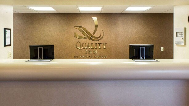 A reception desk with a wall-mounted sign that reads "QUALITY INN BY CHOICE HOTELS". - Quality Inn Brandon - Sioux Falls (Brandon)