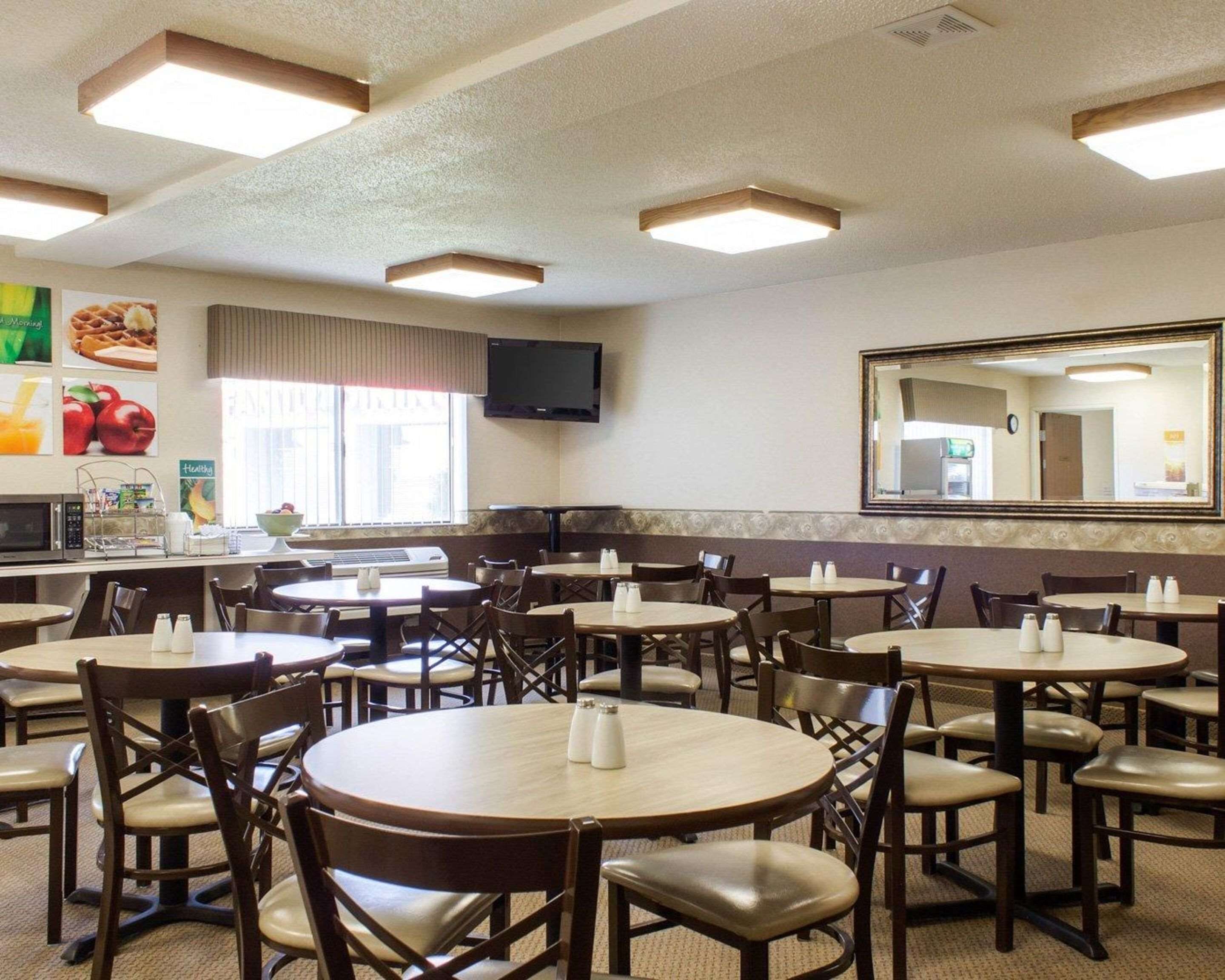 Un restaurante con mesas y sillas redondas, un televisor en la pared y un espejo grande.