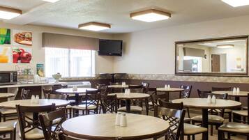 Un restaurante con mesas y sillas redondas, un televisor en la pared y un espejo grande.