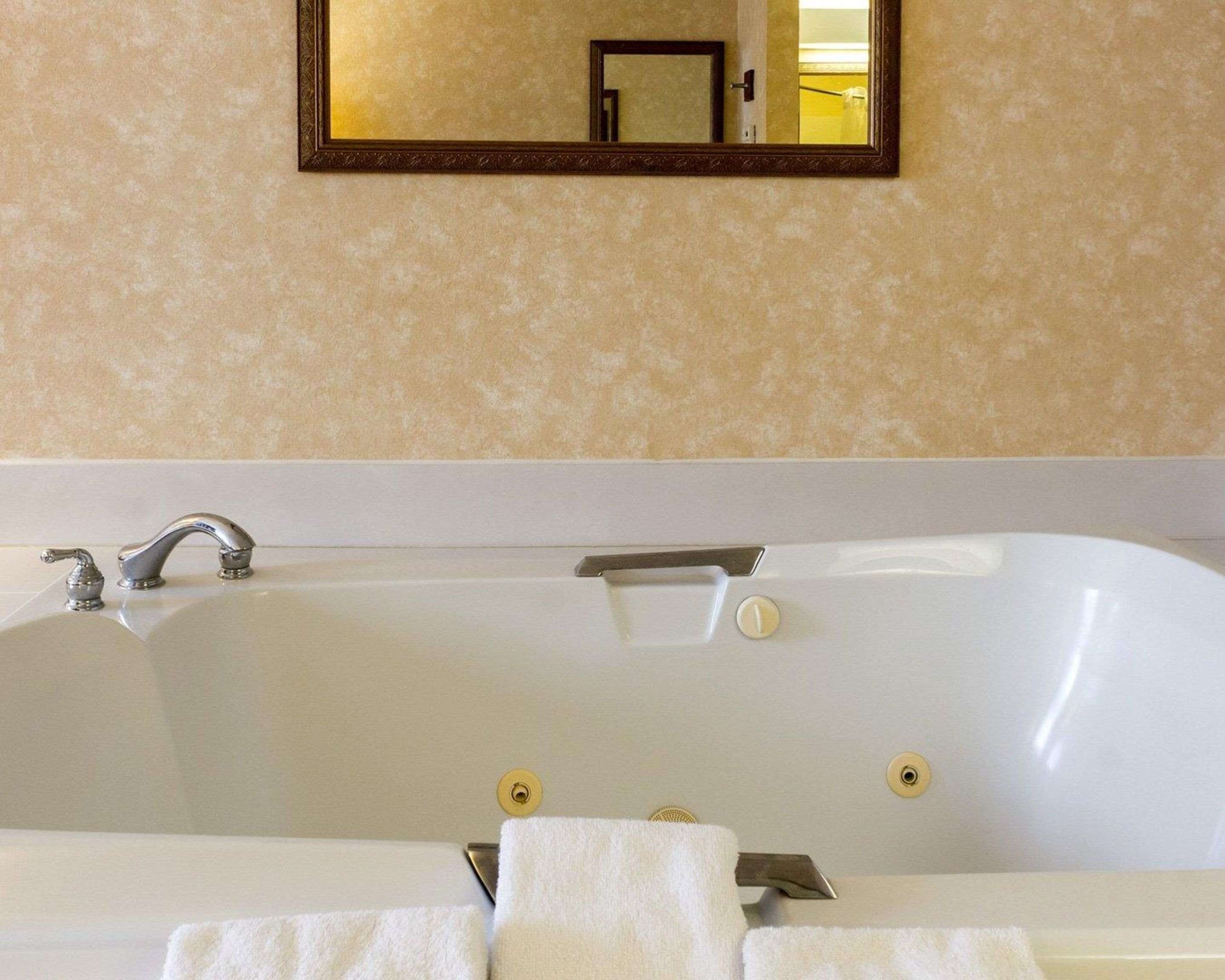 Une salle de bain avec une baignoire blanche, un miroir au-dessus et un porte-serviettes avec deux serviettes.