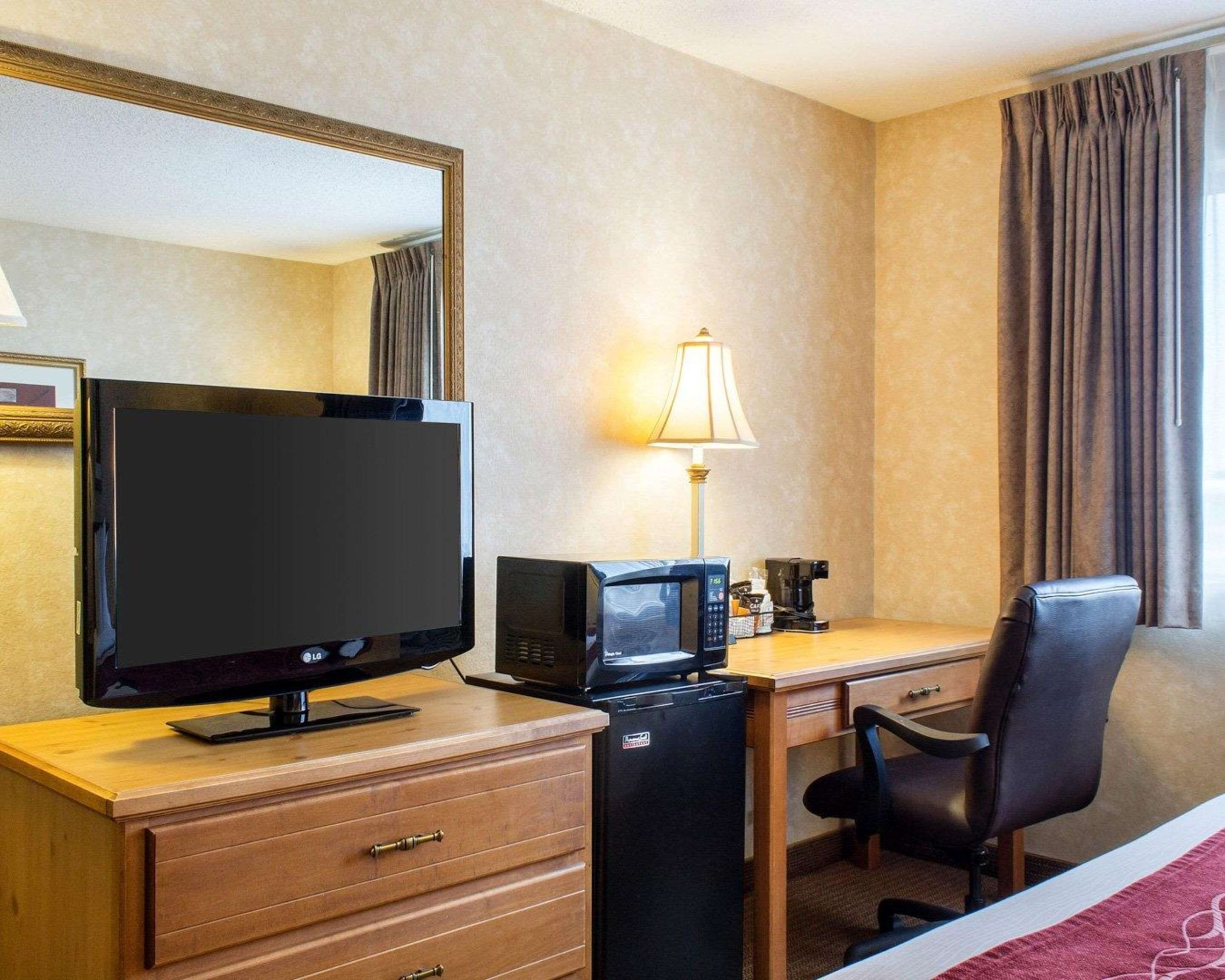A hotel room with a flat-screen TV, a microwave, a coffee maker, a desk, a chair, and a bed.