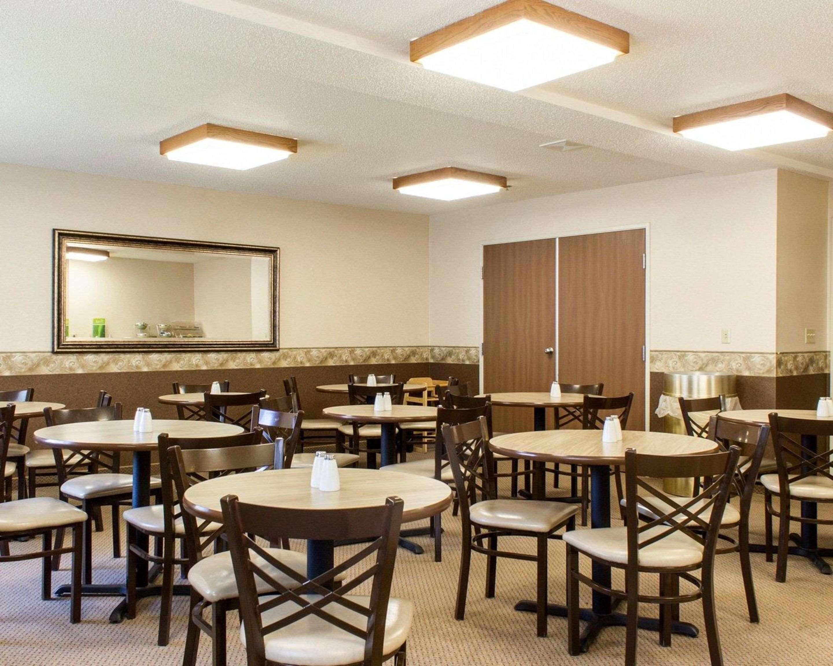 A hotel room with multiple round tables and chairs, a large mirror, and a wardrobe.