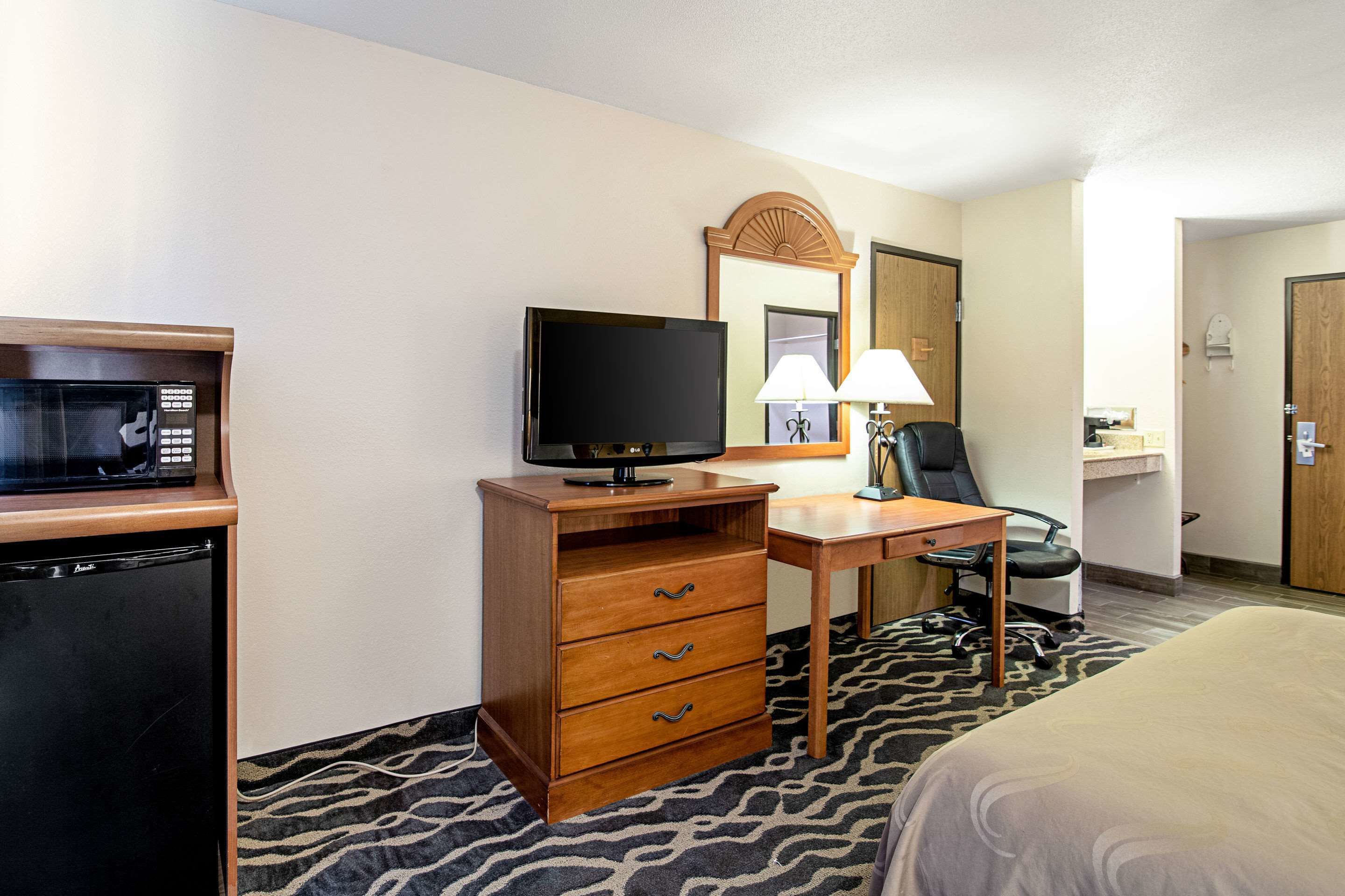 Une chambre d’hôtel comprenant un lit, un bureau avec une chaise, une télévision, un four à micro-ondes et une commode.