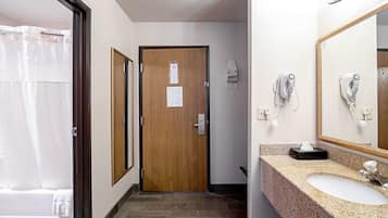 A hotel bathroom with a wooden door, a sink with a mirror, and a shower curtain.