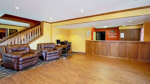 A lobby with a reception desk, leather sofas, a staircase, and a wooden floor. - Quality Inn Huron (Huron)