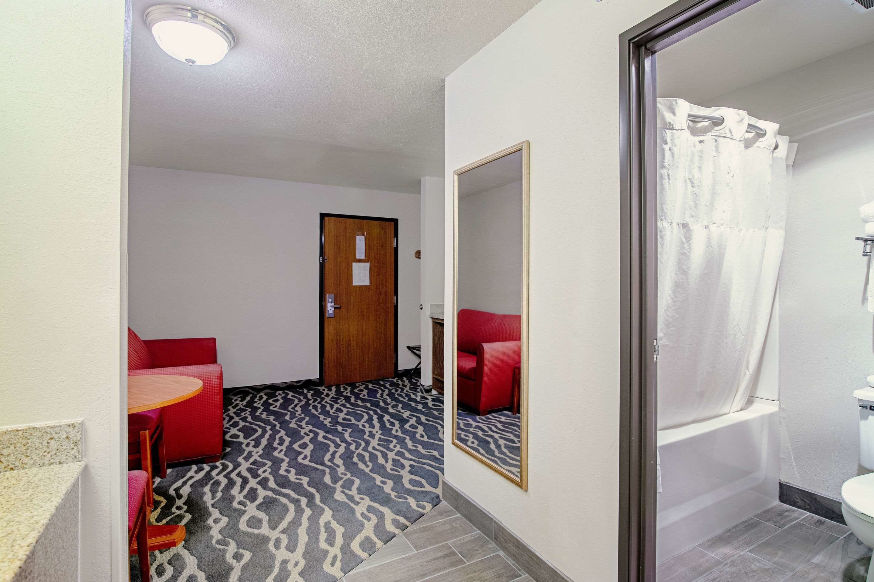 Una habitación de hotel con alfombra estampada, un sofá rojo, una mesita redonda y un espejo en la pared.