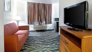 A hotel room with a flat-screen TV, a red sofa, a patterned rug, a wooden dresser, and a window with curtains. - Quality Inn Huron (Huron)