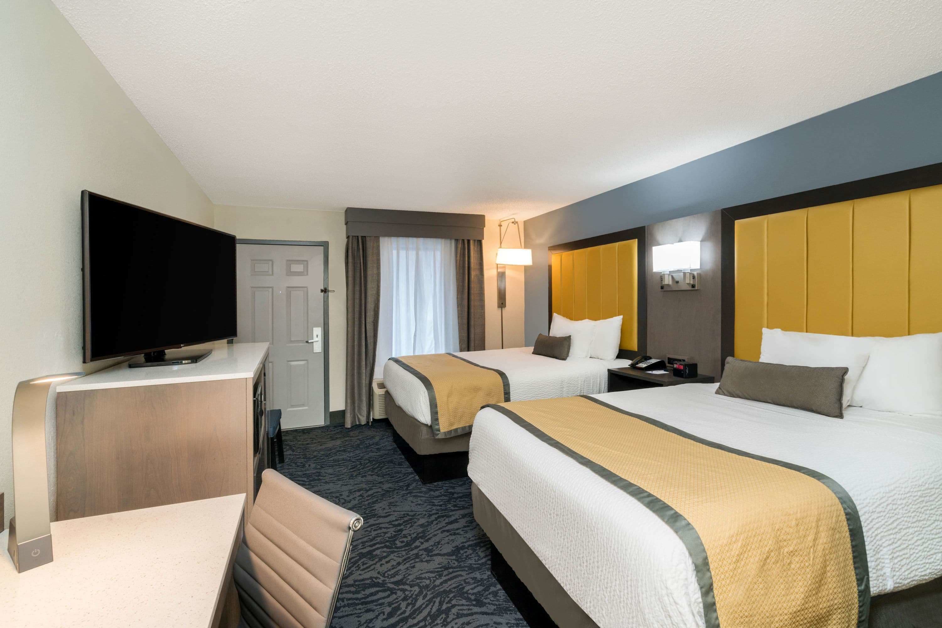 A hotel room with two beds, a TV, a desk, and a chair.
