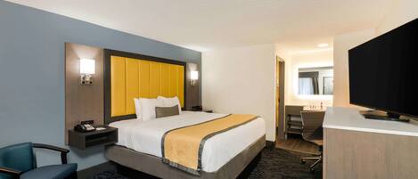 A hotel room with a bed, bedside table, chair, desk, TV, and a bathroom visible through an open door.