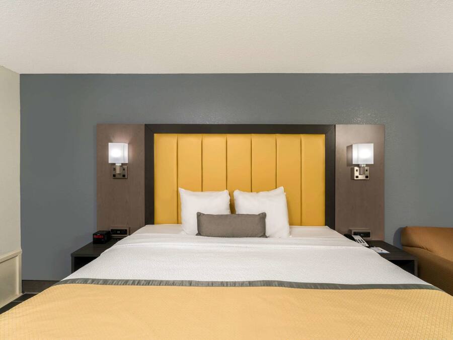 Une chambre d’hôtel avec un grand lit, deux tables de chevet, une petite table, une chaise et une tête de lit dotée d’un éclairage intégré.