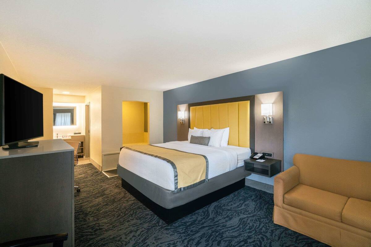 Una habitación de hotel con una cama grande, televisión, escritorio con lámpara y un sofá.