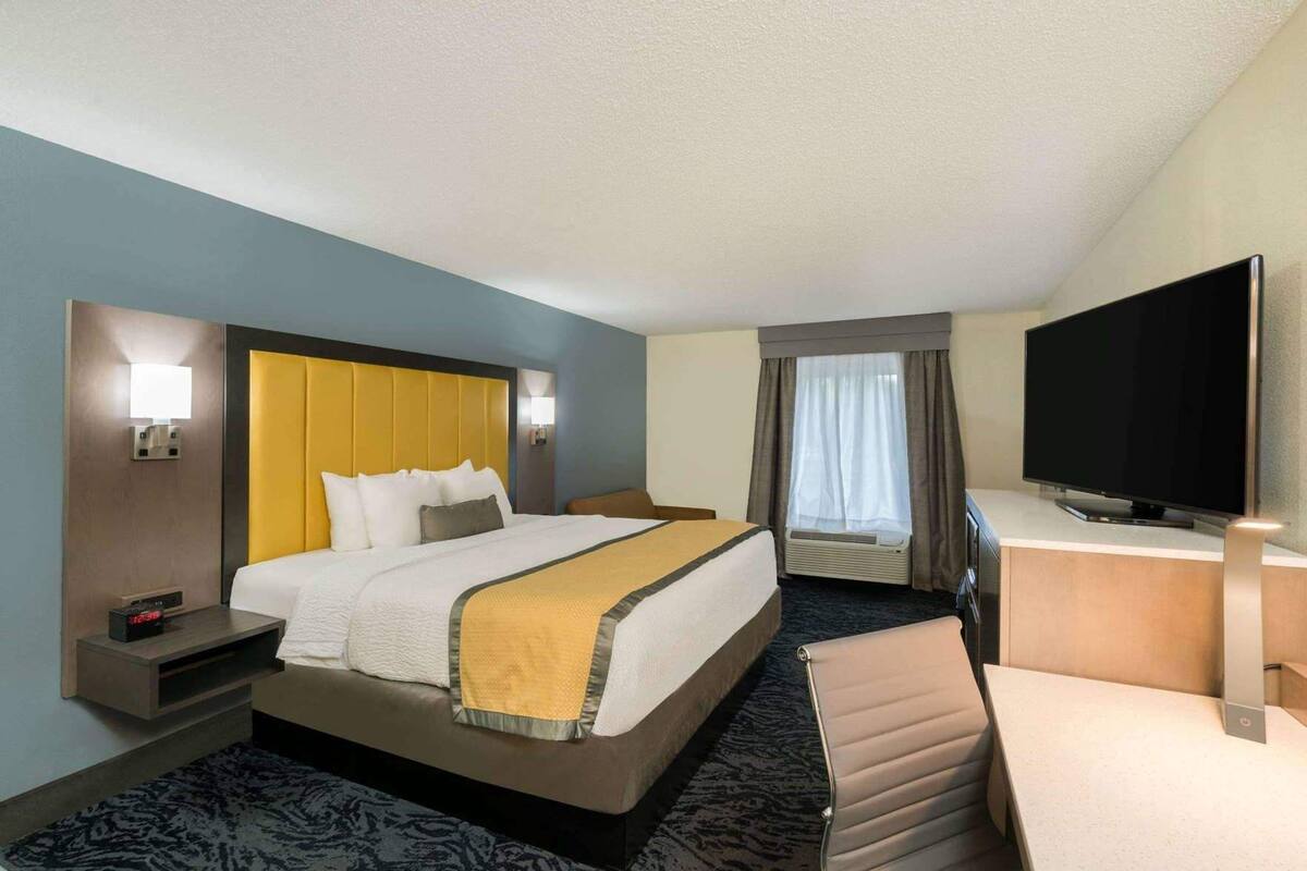 A hotel room with a bed, bedside tables, a desk with a flat-screen TV, a chair, and a window with curtains.