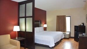 Une chambre d’hôtel comprenant un lit, un bureau, une chaise, une fenêtre avec des rideaux et un mur avec un panneau de verre dépoli.