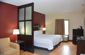 A hotel room with a bed, a desk, a chair, a window with curtains, and a wall with a frosted glass panel. - Red Roof Inn PLUS+ & Suites Chattanooga - Downtown (Chattanooga)