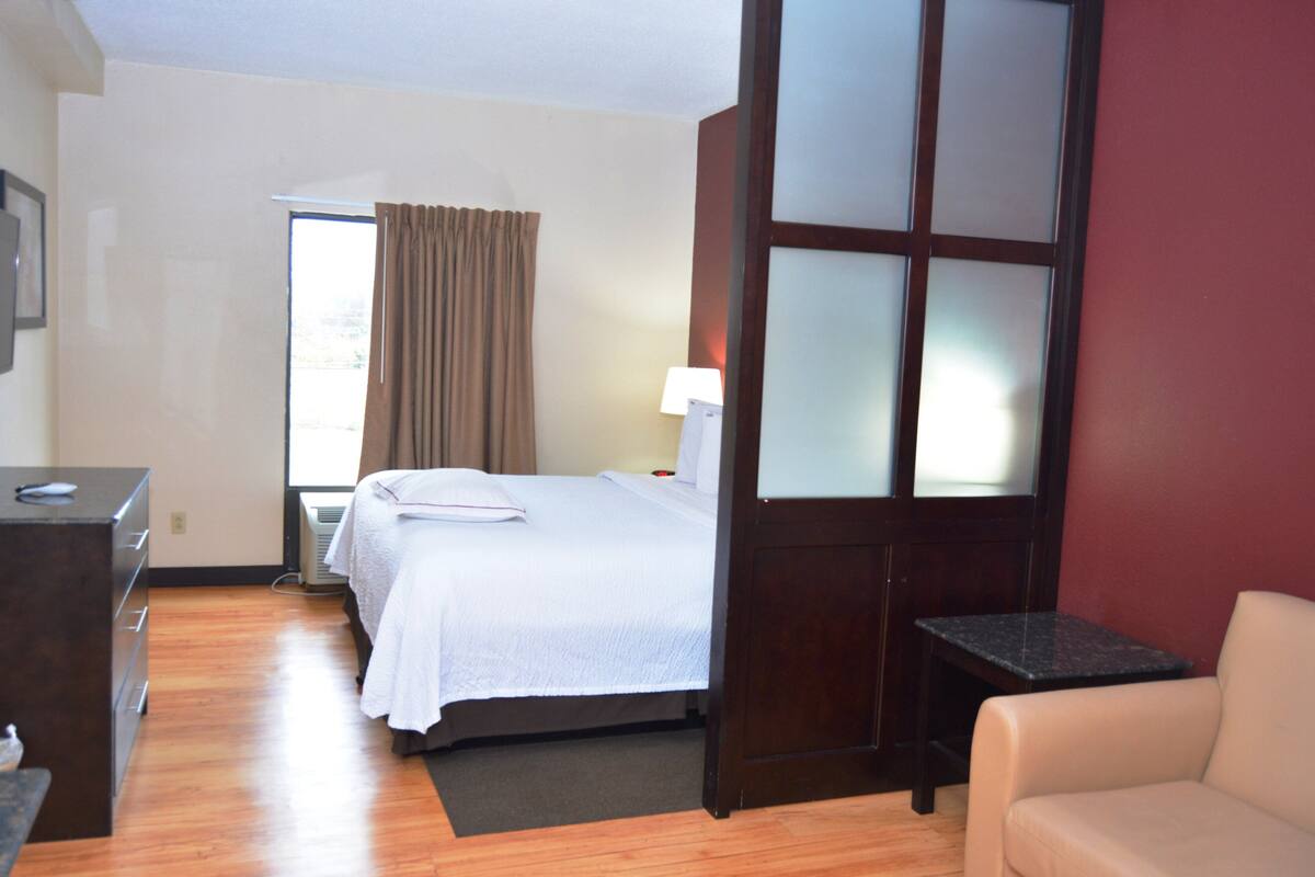 A hotel room with a bed, a desk, a chair, and a small table.