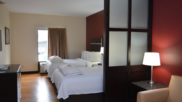 Une chambre d’hôtel avec deux lits, un bureau, une chaise, une lampe et une fenêtre avec des rideaux.