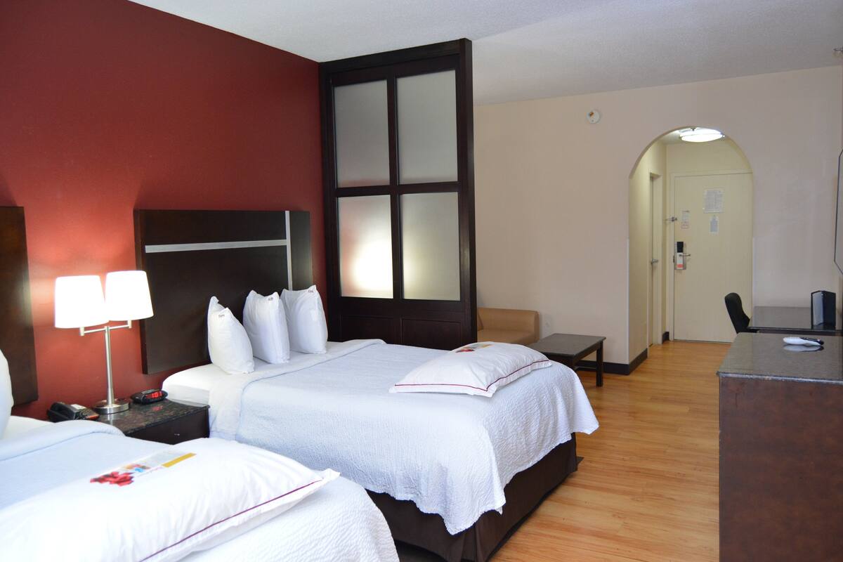 A hotel room with two beds, a desk, and a small seating area.