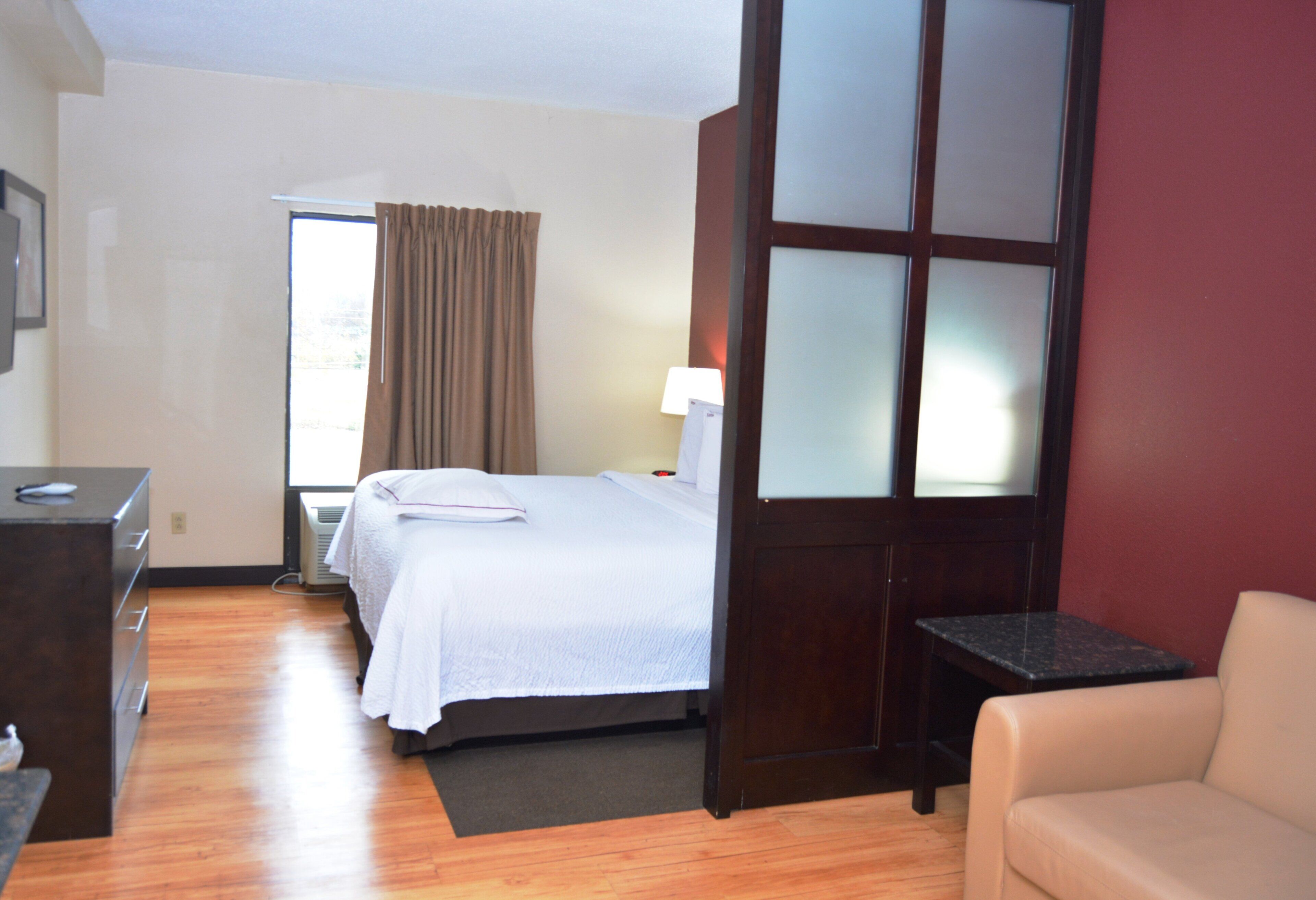 Ein Hotelzimmer mit Bett, Nachttisch, Lampe und Blick ins Freie durch ein Fenster.