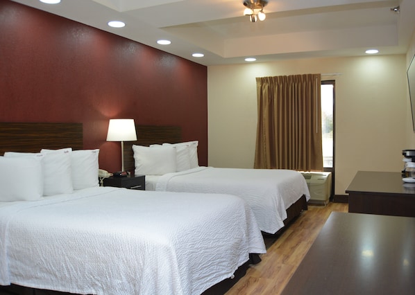 A hotel room with two beds, a desk, a lamp, and a window with curtains.