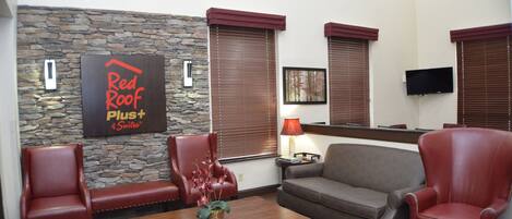 A furnished living area with a stone accent wall, a Red Roof Plus Suites sign, a flat-screen TV, and a coffee table with a floral arrangement.