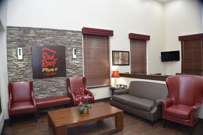 A furnished living area with a stone accent wall, a Red Roof Plus Suites sign, a flat-screen TV, and a coffee table with a floral arrangement. - Red Roof Inn PLUS+ & Suites Chattanooga - Downtown (Chattanooga)