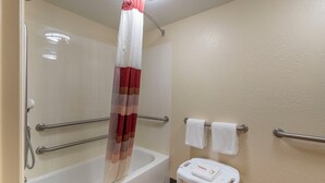 Une salle de bain avec une baignoire blanche, un rideau de douche, un petit tabouret blanc et deux barres d’appui.