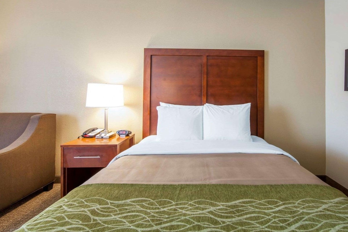 A hotel room with a bed, a nightstand with a lamp, and a chair.