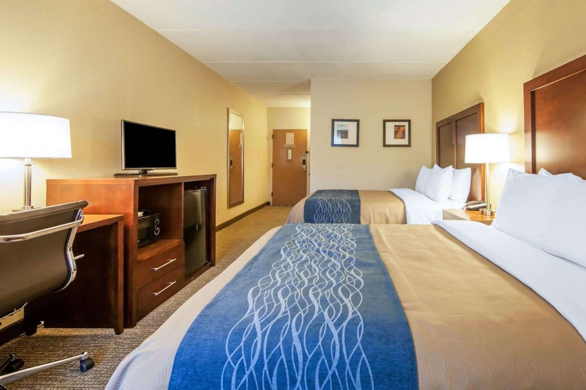 A hotel room with two beds, a desk with a television, a desk lamp, a chair, and a refrigerator.
