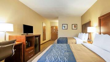 Een hotelkamer met twee bedden, een bureau met een televisie, een bureaulamp, een stoel en een koelkast.
