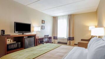 A hotel room with a bed, a desk, a television, and a window with curtains.