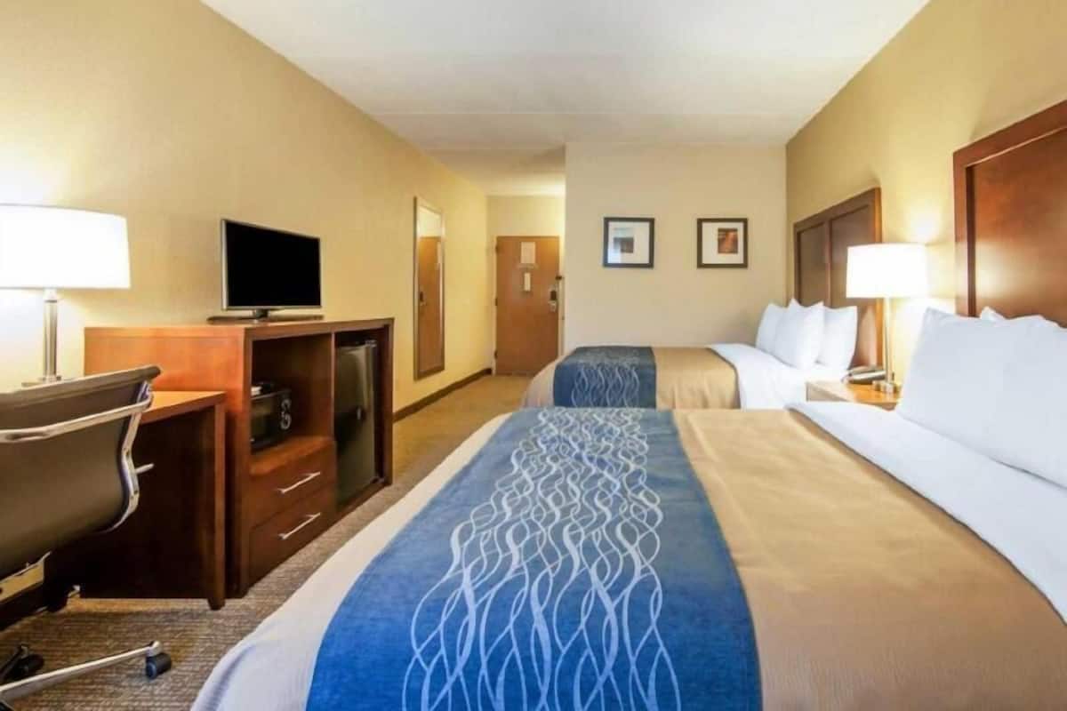 A hotel room with a desk, television, two beds, and a bathroom door.