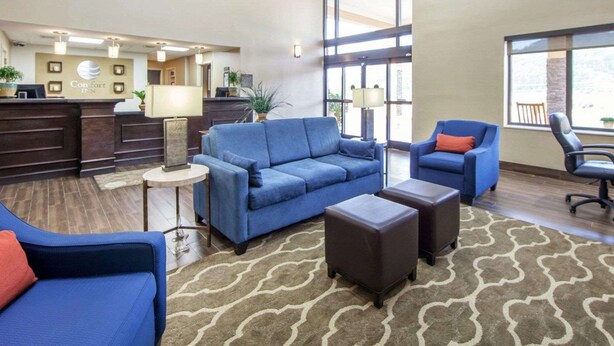 A hotel lobby with a reception desk, seating area with sofas and ottomans, large windows, and a patterned rug. - Comfort Inn at Royal Blue (Pioneer)