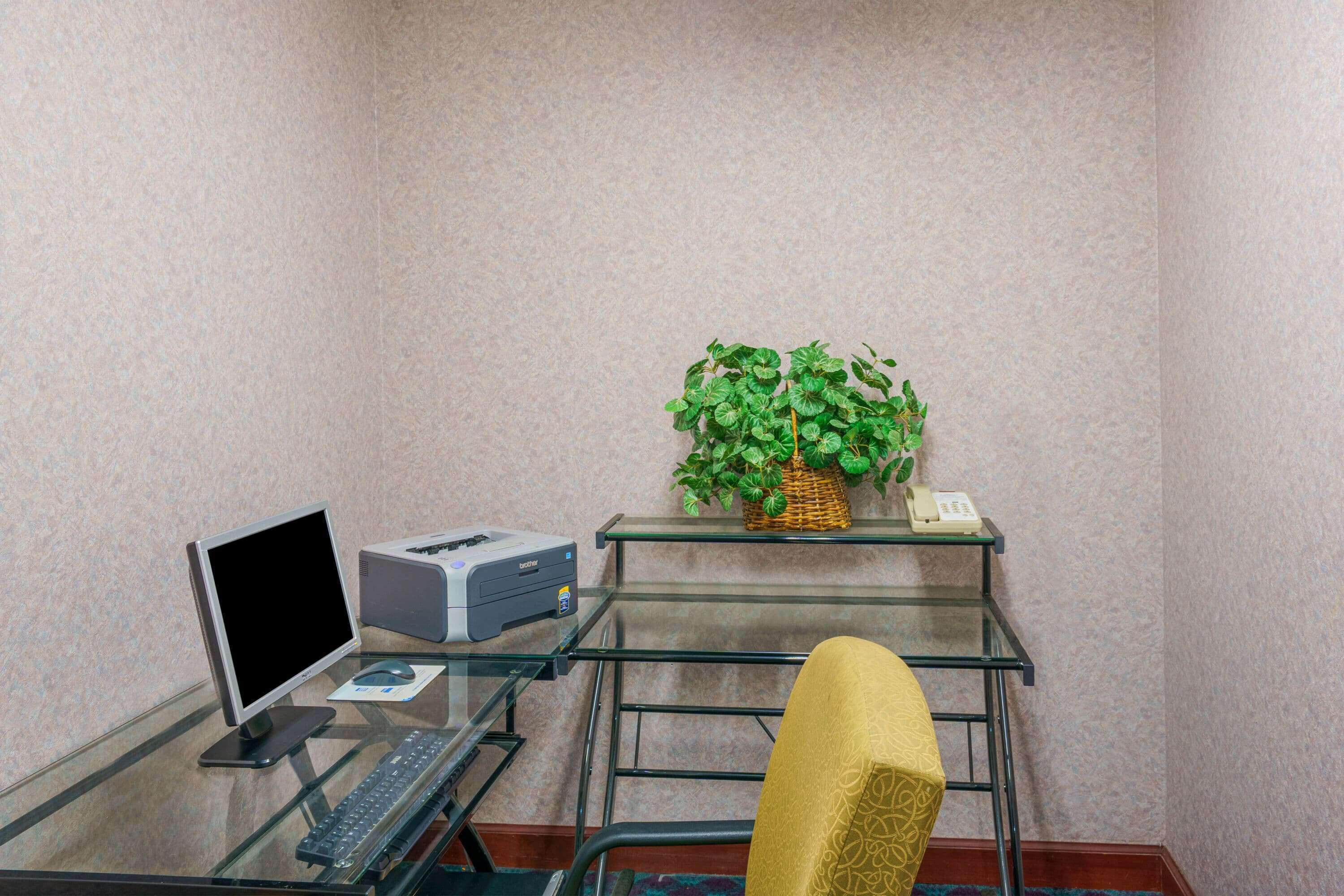 Un pequeño espacio de oficina con una computadora, una impresora y una planta en un estante de vidrio.