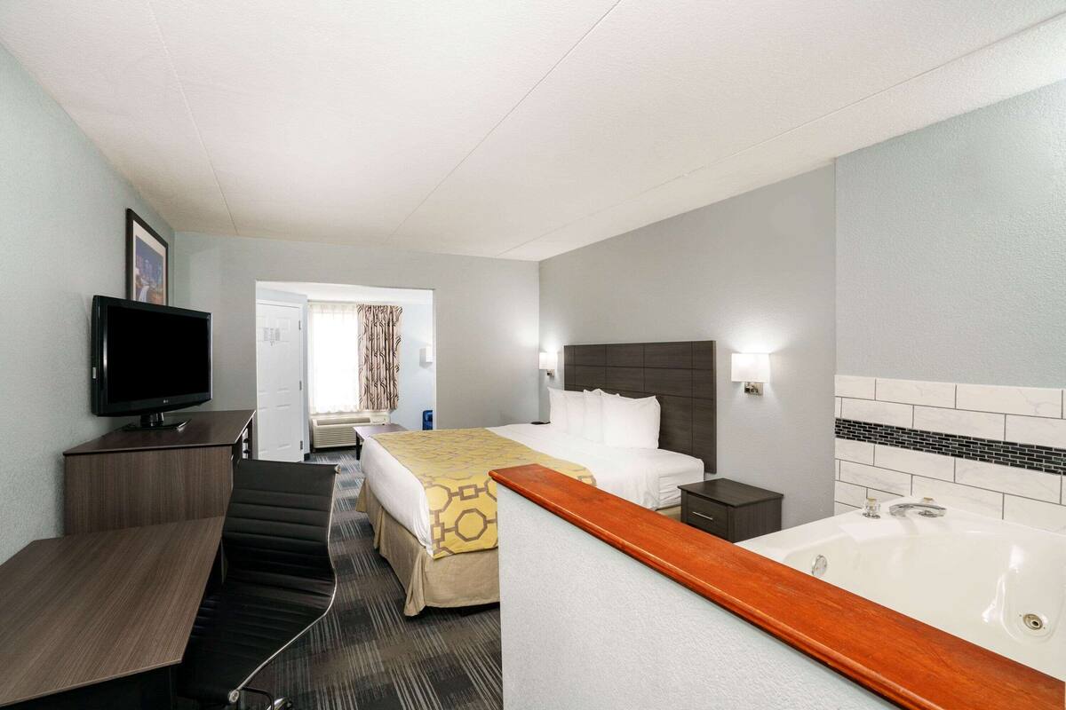 Een hotelkamer met een bed, een bureau, een televisie, een badkamer met bad en een deur naar een andere kamer.