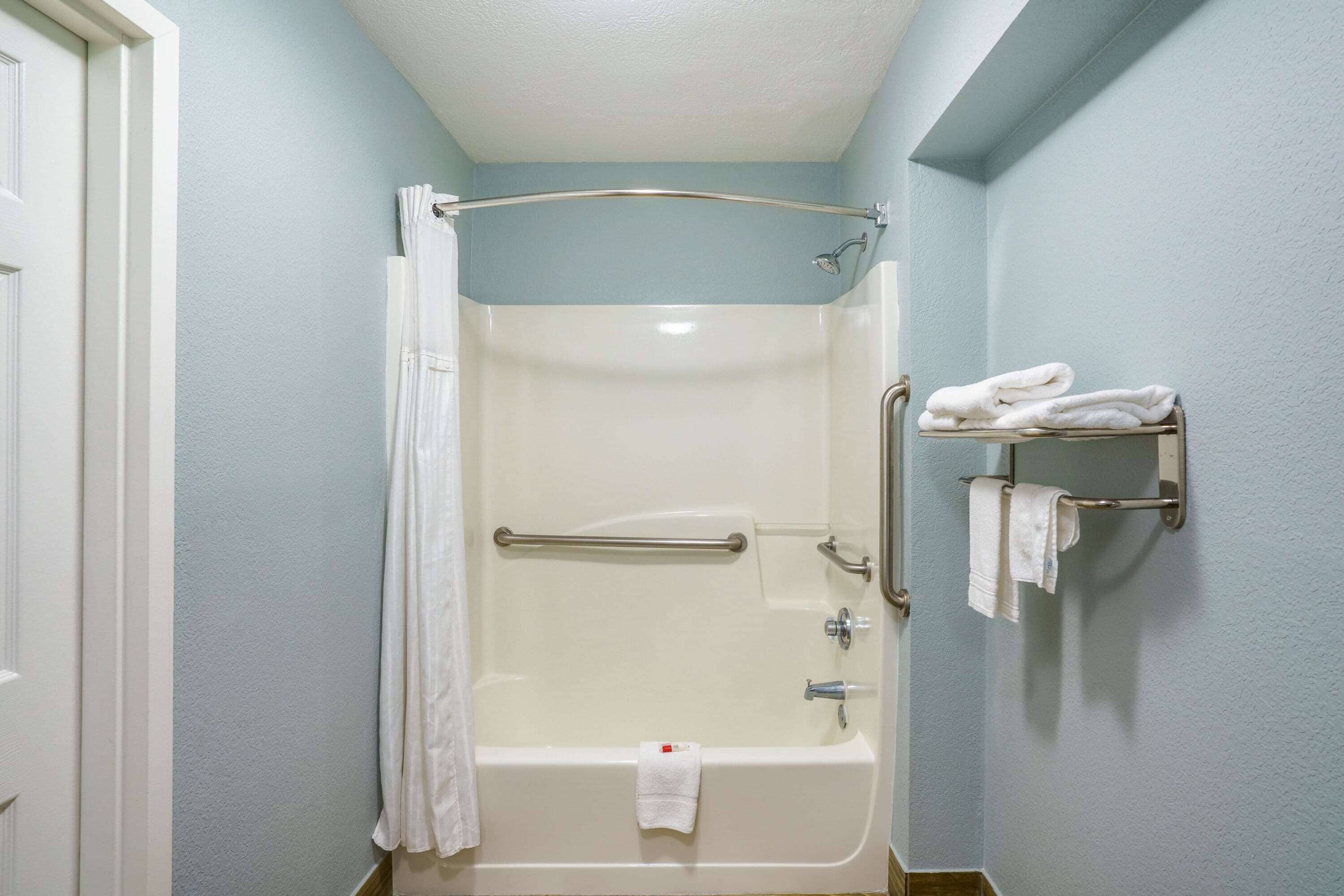 A bathroom with a bathtub, a shower curtain, a towel rack with towels, and a door.