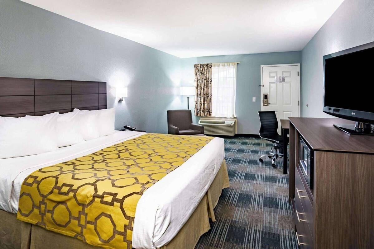 Een hotelkamer met een groot bed, een bureau, een stoel, een televisie en een raam met gordijnen.