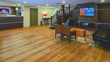Un vestíbulo de hotel con mostrador de recepción, una escalera y un área de estar con una mesa de centro y sillas.