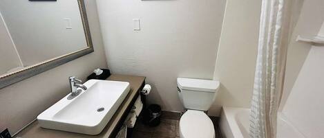 Un baño con lavamanos, inodoro y bañera blancos. Hay cuadros enmarcados en la pared.