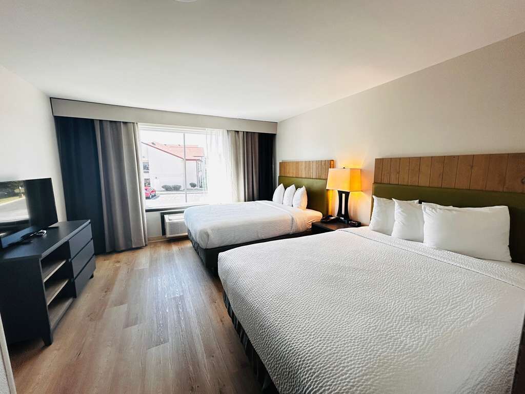 A hotel room with two beds, a TV, a desk, and a window with curtains.