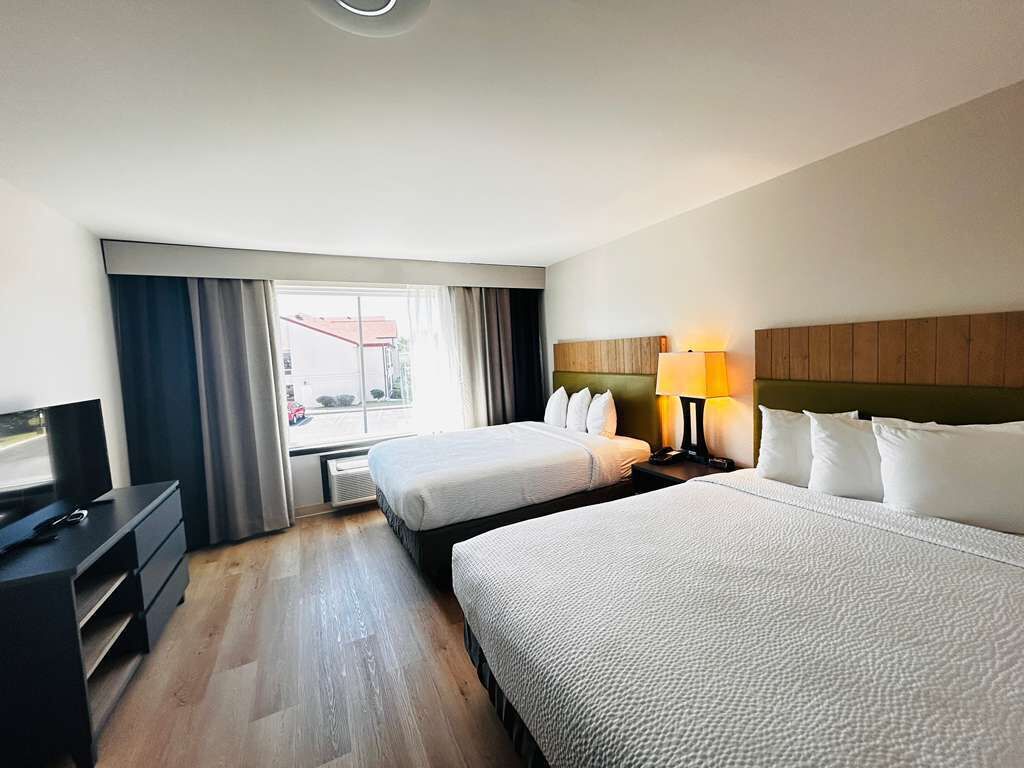 A hotel room with two beds, a desk with a TV, a lamp, and a window with curtains.